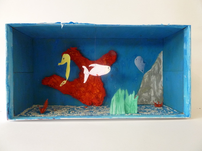 Die Fische h�ngen von der Decke herunter, die Korallen, die am Boden sind, sind kleine �ste, die ich rot angemalt habe. Die gro�e Koralle an der R�ckseite der Schuhschachtel besteht aus Watte, die in Form gebracht und dann in rote Farbe getaucht wurden.